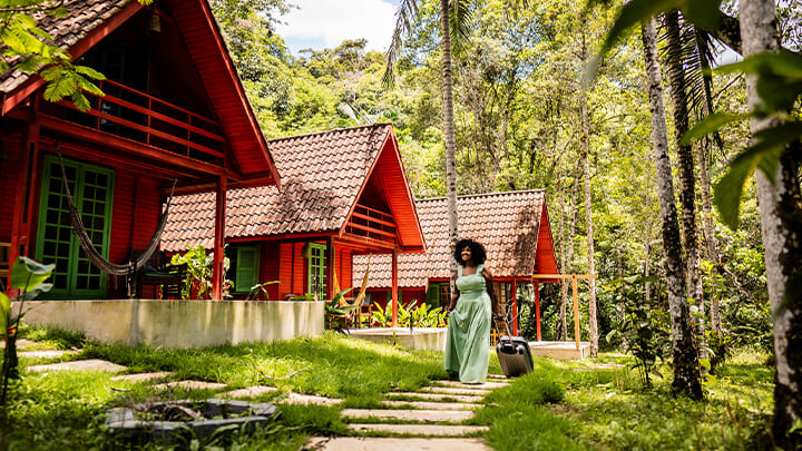 Woman walking in front of cottages in a densely forested area